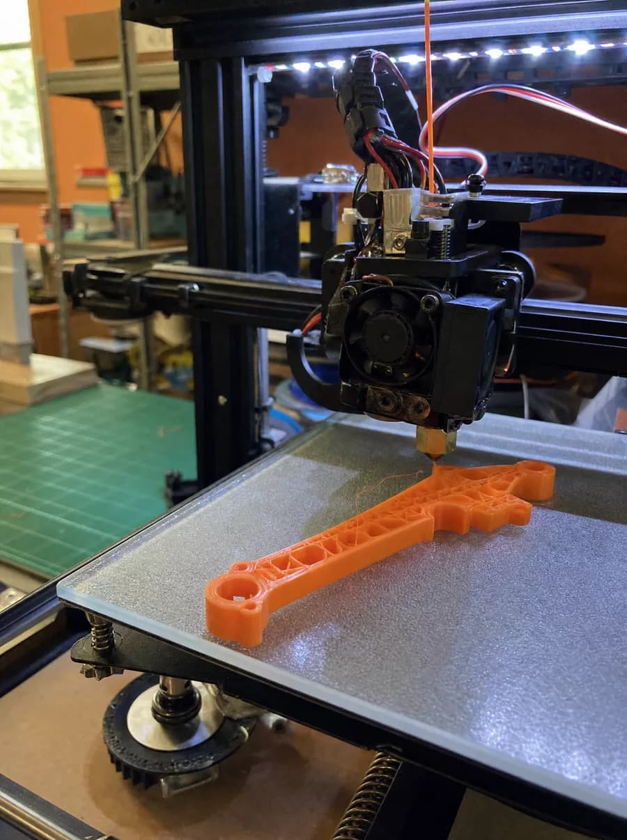 Atölyedeki 3D baskı istasyonunda üretilen turuncu İHA gövde parçası ve baskı kafası